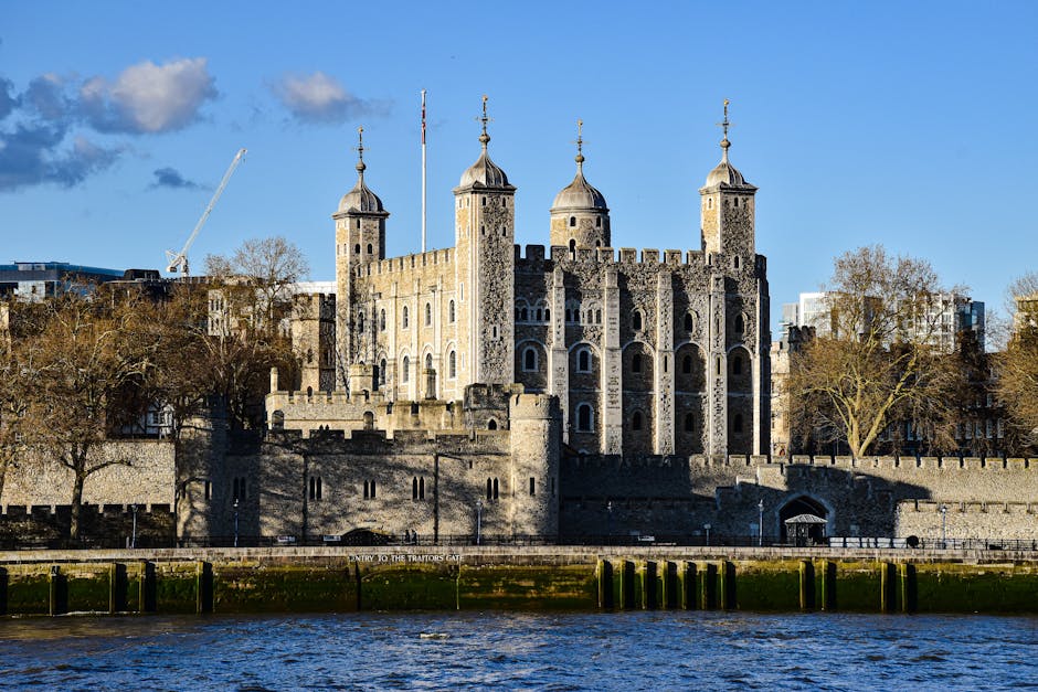 A detailed view of the Tower of London, an historic stone fortress with high stone walls, four prominent towers topped with conical roofs, and crenellated battlements, situated on the north bank of th